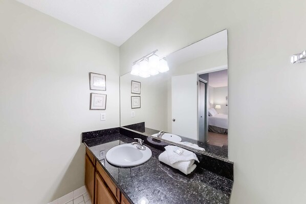 A bathroom with a sink, mirror, and framed pictures on the wall. - Cheerful Condo with Shared Pool, Pier, and Beach Access (Gulf Shores)