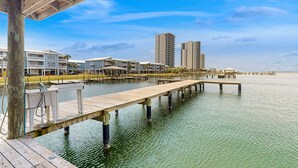 Een pand aan het water met een houten steiger die het water in reikt, omringd door moderne gebouwen en een heldere lucht.