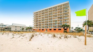 Een hotel aan het strand met meerdere balkons, een zandstrand ervoor en een groene vlag.