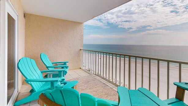 Een balkon met turquoise Adirondack-stoelen, uitzicht op het strand en een leuning.
