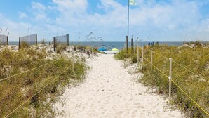 Een zandpad langs het strand dat naar de zee leidt, met een vlaggenmast en een hek.