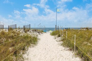 Ein sandiger Strandweg führt zum Meer, mit einer Fahnenmast und einem Zaun.