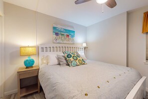 A bedroom with a bed, nightstands, a ceiling fan, and a beach-themed painting. - Gorgeous Beach Home Overlooking the Beach w/Free WiFi, Central AC, Shared Pool and Covered Parking (Gulf Shores)