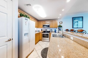 Una cocina con gabinetes de madera, un refrigerador de acero inoxidable, un microondas, un horno, un lavaplatos y una encimera de granito.