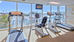 Ein Fitnessraum mit Laufbändern, einem Crosstrainer und einem Hometrainer, inklusive Fernsehbildschirm und großen Fenstern mit Aussicht auf eine schöne Landschaft.