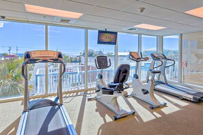 A gym with treadmills, an elliptical, and a stationary bike, with a TV screen and large windows overlooking a scenic view. - Wonderful Gulf Shores Home with Fantastic Water Views, Free WiFi, Shared Pool,Sauna (Gulf Shores)