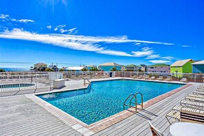 Una piscina con muelle de madera, un puesto de socorrista y sillas de descanso.