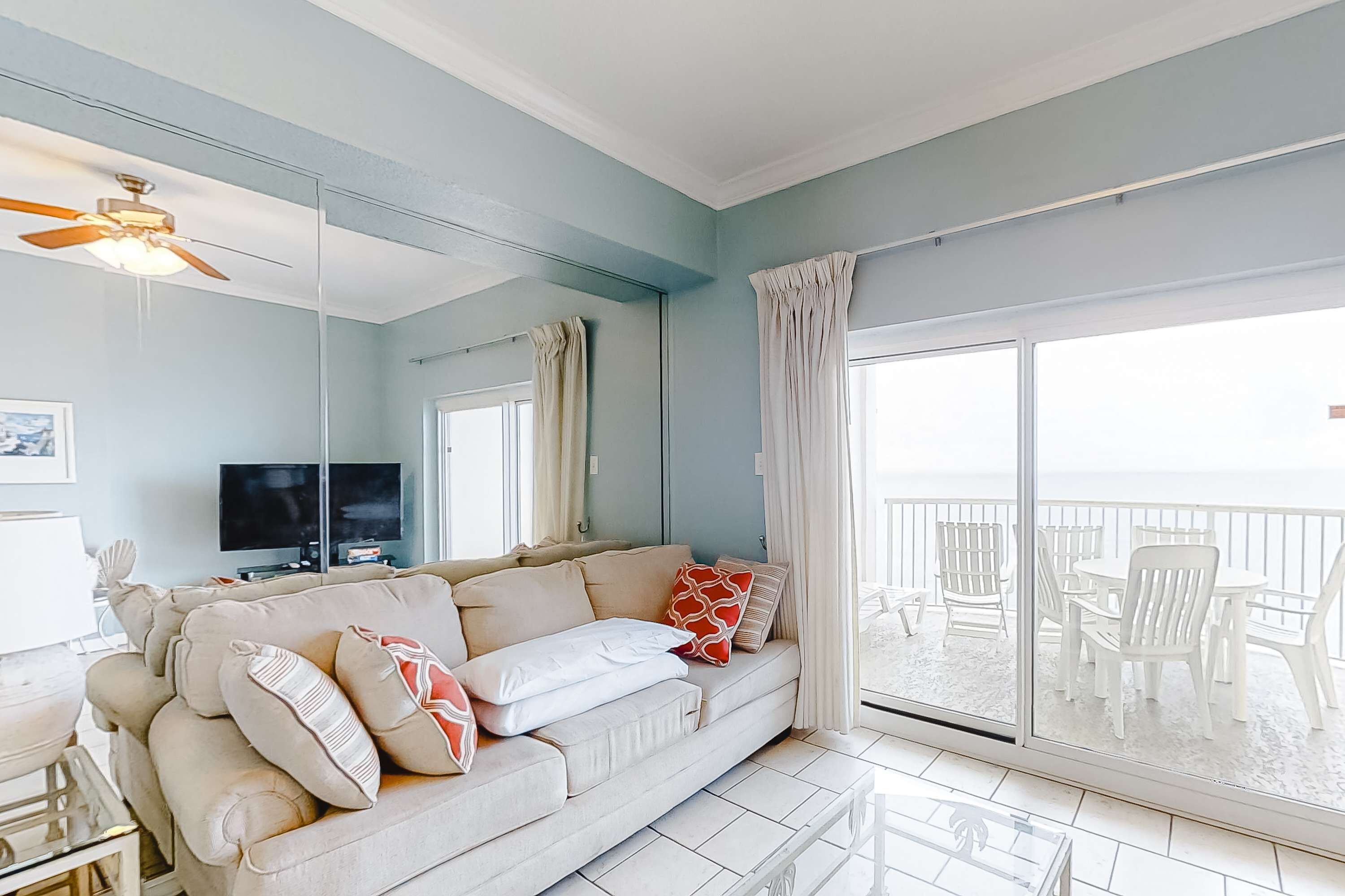 A living room with a sofa, TV, and balcony with white furniture.