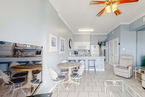 Eine kompakte Küche mit weißen Schränken, ein Essbereich mit rundem Tisch und Stühlen sowie ein Deckenventilator.