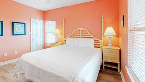 Une chambre à coucher avec un lit, deux tables de chevet avec des lampes, une porte et une fenêtre avec des stores.