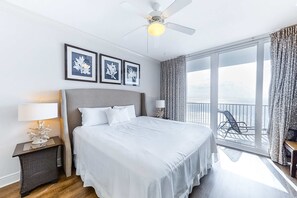 Une chambre d’hôtel avec un grand lit, un ventilateur de plafond, un balcon avec une chaise et des œuvres d’art encadrées accrochées au mur.