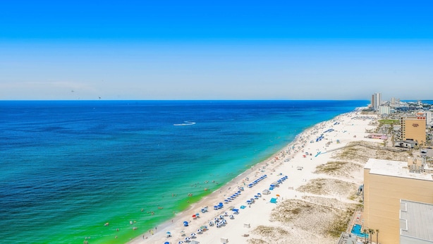 Una spiaggia con acqua cristallina, una riva sabbiosa e edifici sullo sfondo.