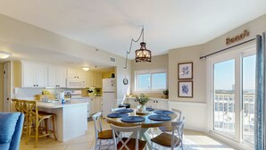 A modern kitchen with white cabinets, a central island, and a dining area with a round table and chairs. - Gulfview condo wbalcony & resort amenities - shared pools, hot tubs, tennis (Gulf Shores)