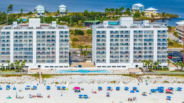 Ein Strandhotel mit mehreren Hochhäusern, einem Schwimmbad und einem Strandbereich mit Sonnenschirmen und Liegestühlen.