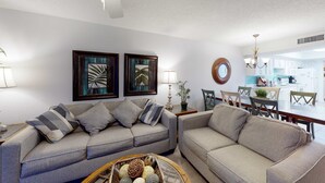Ein Wohnzimmer mit zwei Sofas, einem Esstisch, Stühlen, einer Lampe und gerahmten Kunstwerken an der Wand.