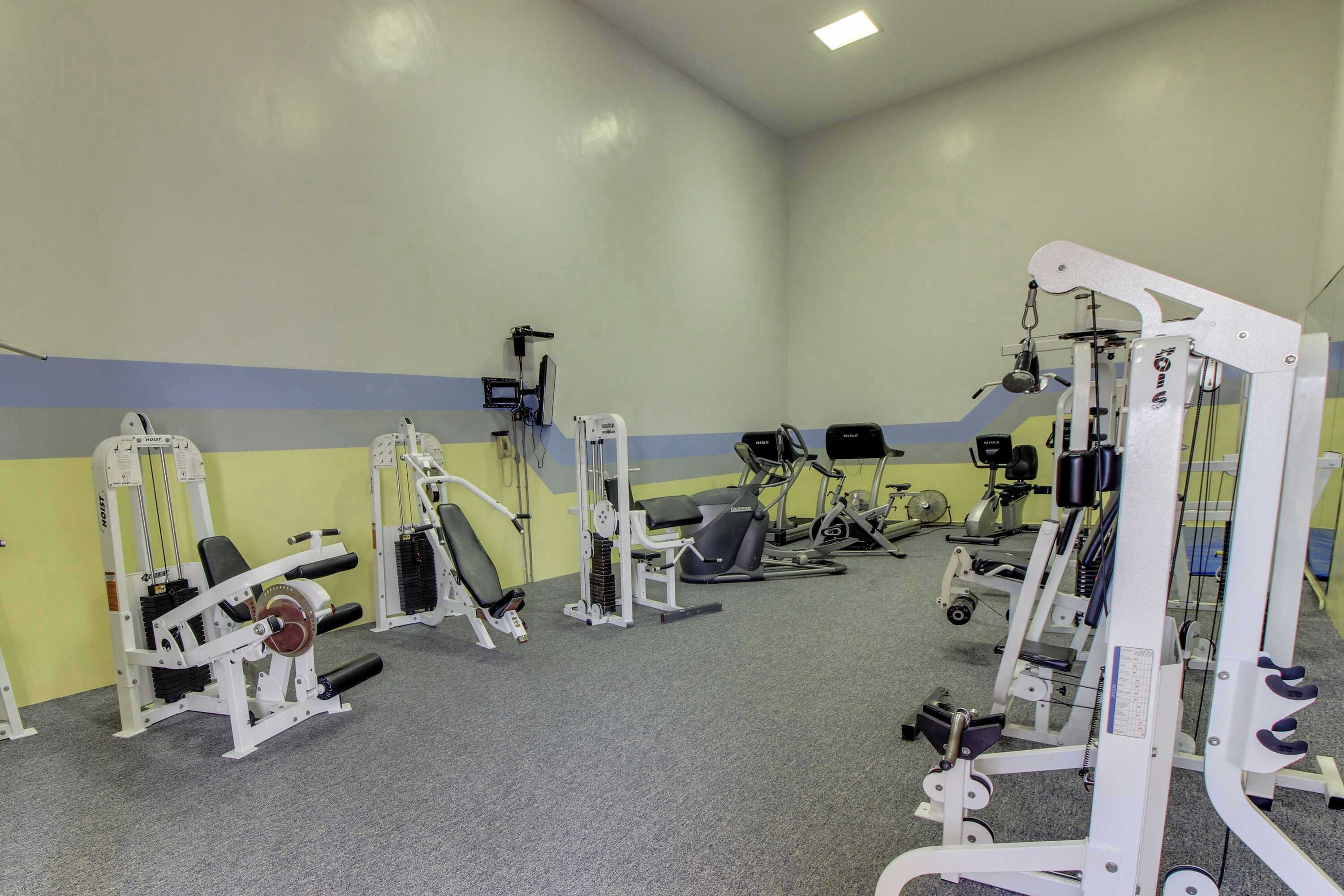 Ein Fitnessraum mit verschiedenen Trainingsgeräten, einer Bank und einem an der Wand montierten Fernseher.