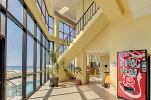 A hotel lobby with a pool, large windows, a Coca-Cola vending machine, and a staircase. - Waterfront condo with amazing views, beach access & pool/hot tub on-site (Orange Beach)