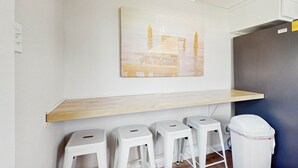Ein Zimmer mit einem Holzregal, weißen Hocker, einer weißen Mülltonne und einem Bild von einem Steg.