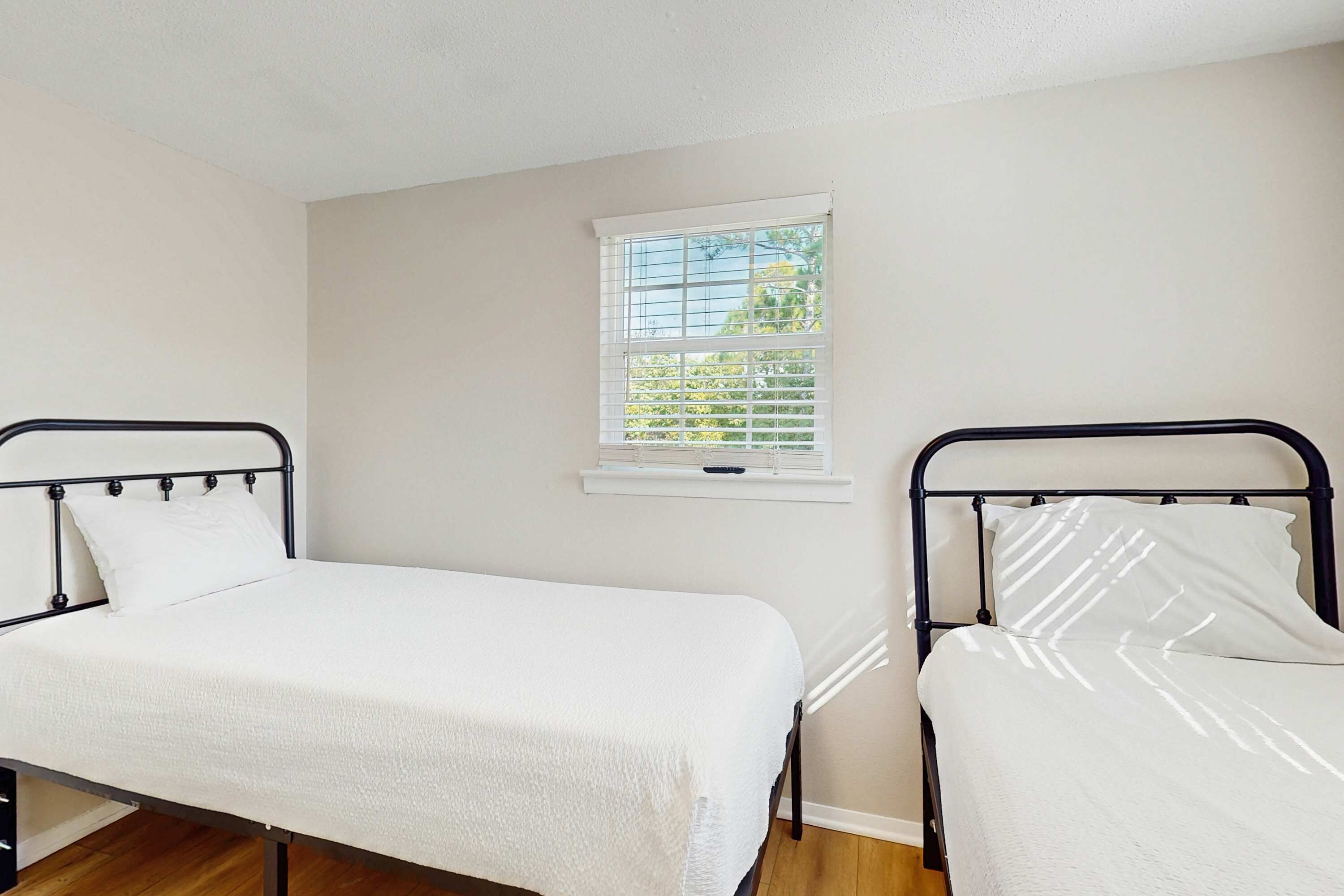 Une chambre avec deux lits simples, une fenêtre avec des stores et un mur blanc.