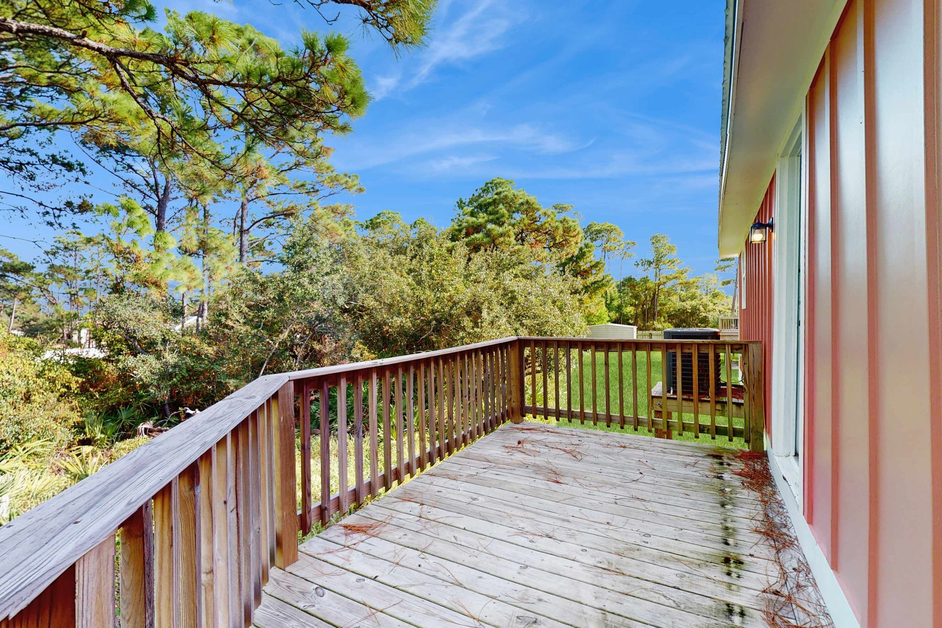 Une terrasse en bois avec une rambarde, entourée d’arbres et sous un ciel dégagé.