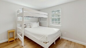 En våningssäng med en träram och vitt sänglinne, en liten träpall, ett fönster med persienner och en taklampa.