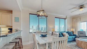 A modern kitchen with a dining area, a blue sofa, and a city view. - Beachview condo with shared indoor and outdoor pool, beach acces, and WIFI (Gulf Shores)