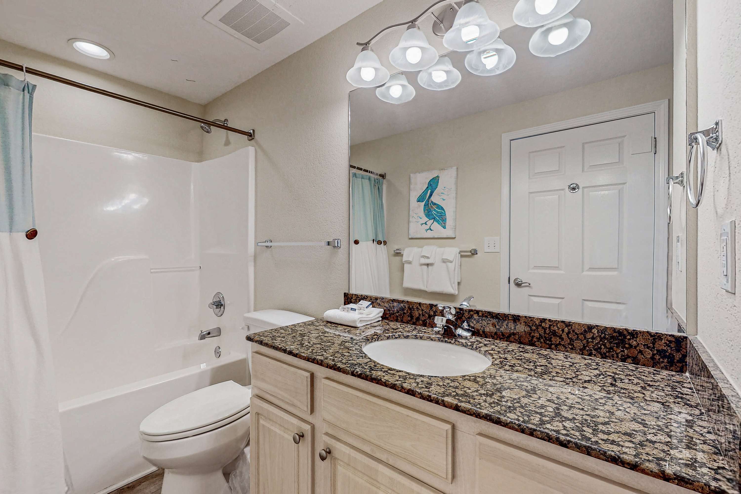 A bathroom with a bathtub, toilet, sink, vanity, and a large mirror.