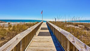A wooden boardwalk leading to a beach with a flag. - Beachview condo with shared indoor and outdoor pool, beach acces, and WIFI (Gulf Shores)