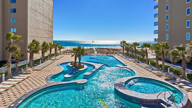 A resort with a pool area, palm trees, and a view of the beach. - Beachview condo with shared indoor and outdoor pool, beach acces, and WIFI (Gulf Shores)