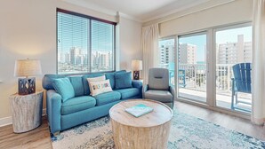 A living room with a sofa, armchair, round coffee table, and a view of the city through large windows. - Beachview condo with shared indoor and outdoor pool, beach acces, and WIFI (Gulf Shores)
