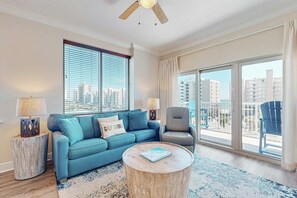 Ein Wohnzimmer mit Sofa, Ohrensessel, rundem Couchtisch und Blick auf die Stadt durch große Fenster.