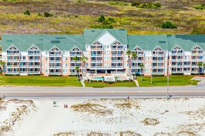 Ein Hotel direkt am Strand mit mehreren Balkonen, einem Schwimmbad und einer grünen Rasenfläche.
