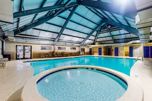 An indoor swimming pool with a high ceiling and a sunroof, surrounded by lounge chairs and a changing room area. - Bright coastal condo with Gulf views, pools, hot tub & private balcony (Gulf Shores)