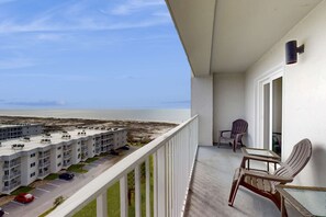 A balcony with a view of a beach, a parking lot, and a building with multiple floors. - Bright coastal condo with Gulf views, pools, hot tub & private balcony (Gulf Shores)
