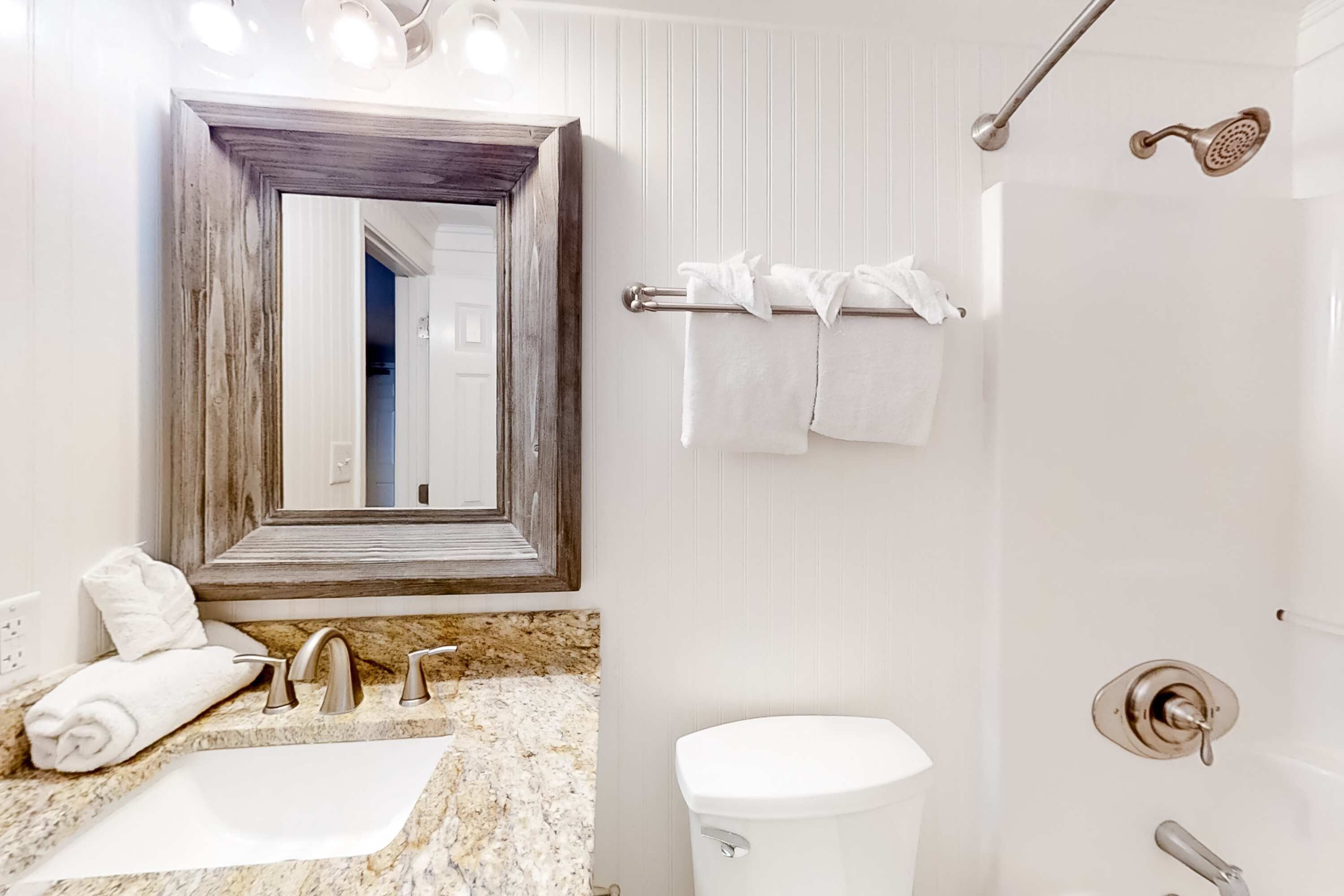 A bathroom with a sink, mirror, towel rack, shower, and toilet.