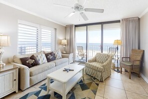 A living room with a sofa, armchair, coffee table, and a large window with a view. - Amazing Condo in Gulf-Front w/Free WiFi, Shared Pool & Hot Tub, Central AC (Orange Beach)
