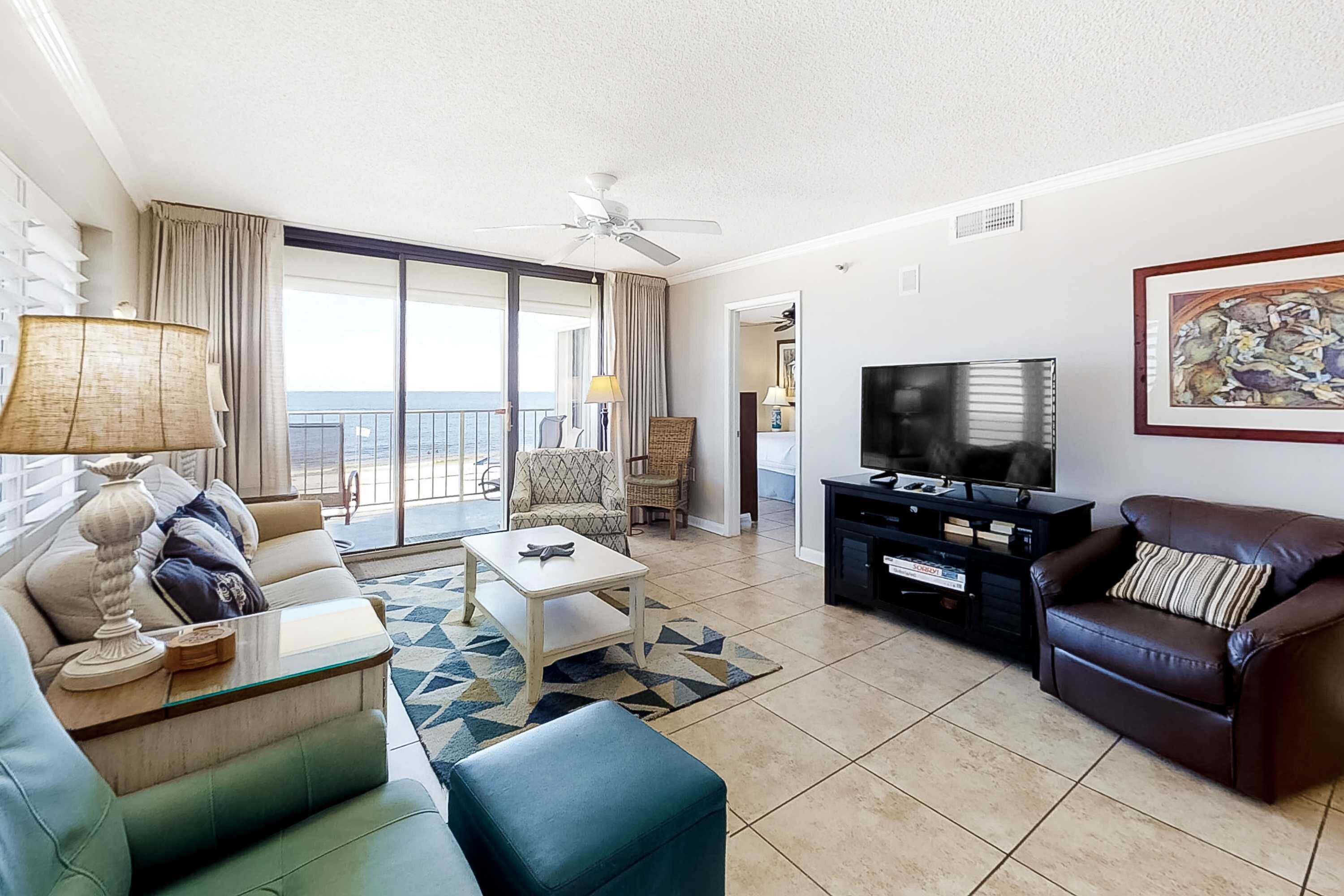 Ein Wohnzimmer mit einer Couch, einem Couchtisch, einem Fernseher und einem Balkon mit Vorhängen.