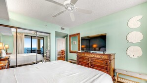 Een hotelkamer met een bed, een televisie, een dressoir en uitzicht op de oceaan.