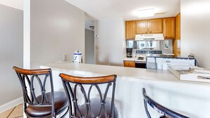 A kitchen with wooden cabinets, a white countertop, and a refrigerator. - Bright resort condo with pool access, cozy patio, plus a washer/dryer (Orange Beach)