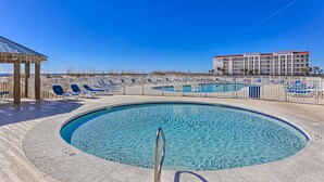 A swimming pool with lounge chairs, a covered area, and a building in the background. - Bright resort condo with pool access, cozy patio, plus a washer/dryer (Orange Beach)