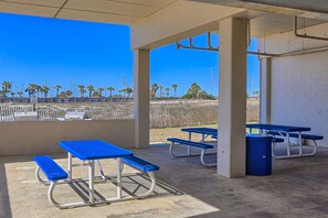 A covered outdoor area with picnic tables and benches, a trash can, and a view of the beach.