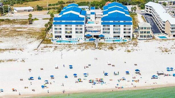 A beachfront hotel with multiple blue-roofed buildings, a sandy beach with umbrellas, and a clear view of the ocean. - Bright resort condo with pool access, cozy patio, plus a washer/dryer (Orange Beach)