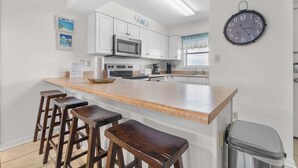 A kitchen with white cabinets, a stainless steel microwave, a coffee maker, and a clock on the wall. - Wonderful home in beachfront complex with pool, WiFi & central AC (Orange Beach)