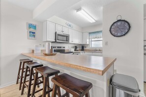Eine Küche mit weißen Schränken, einer Edelstahl-Mikrowelle, einer Kaffeemaschine und einer Uhr an der Wand.