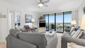A modern living room with grey sofas, a flat-screen TV, and a balcony with a view. - Wonderful home in beachfront complex with pool, WiFi & central AC (Orange Beach)