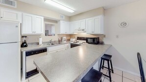 A kitchen with white cabinets, a granite countertop, a dishwasher, a microwave, and a clock on the wall. - Wonderful beachfront vacation complex with private pool, WiFi, balcony & AC (Orange Beach)