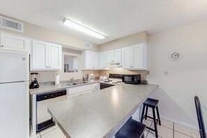 A kitchen with white cabinets, a granite countertop, a dishwasher, a microwave, and a clock on the wall. - Wonderful beachfront vacation complex with private pool, WiFi, balcony & AC (Orange Beach)