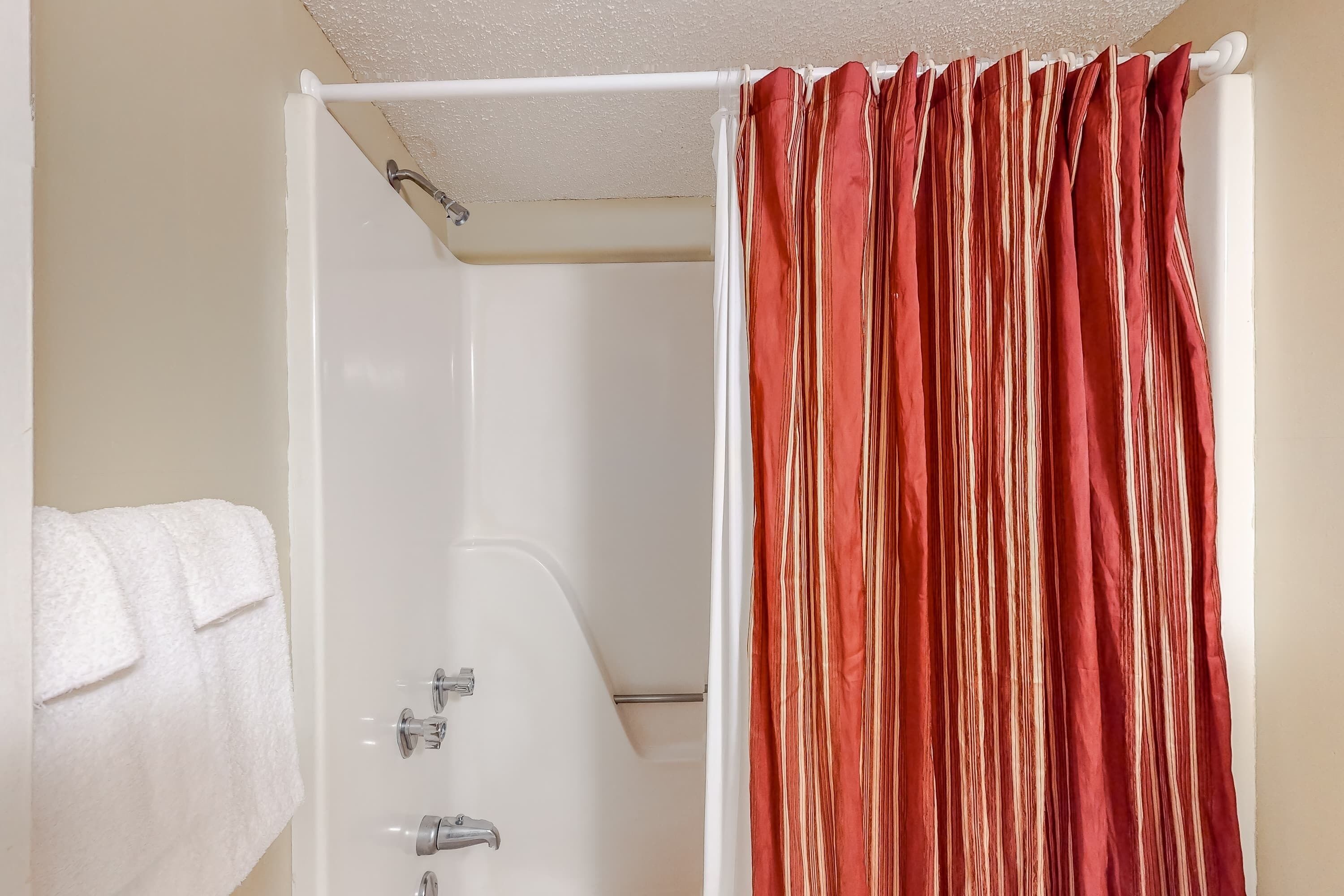 A bathroom with a white bathtub, a white towel, and a red-striped shower curtain.