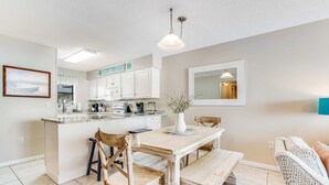 A kitchen with white cabinets, a wooden dining table, and a bench. - Beautiful home in beachfront luxury complex with pool, sauna & WiFi (Orange Beach)