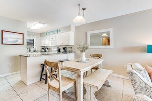 A kitchen with white cabinets, a wooden dining table, and a bench. - Beautiful home in beachfront luxury complex with pool, sauna & WiFi (Orange Beach)